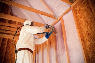 Worker installing spray foam insulation in a wall and ceiling.