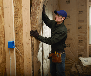 Worker installing kraft-faced fiberglass insulation in a wall.
