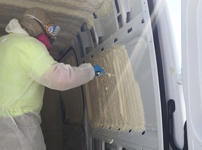 Worker installing spray foam insulation in a van.