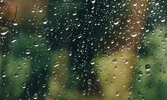 Raindrops splattered on a window with blurred green background.