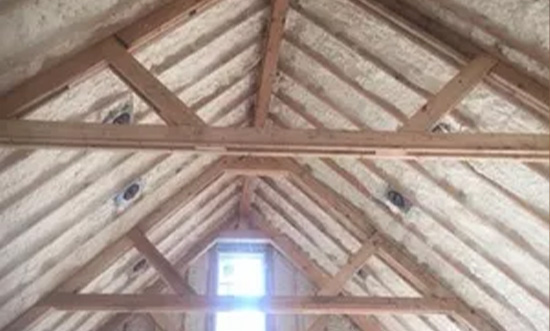Exposed wooden beams and insulation in an unfinished attic.