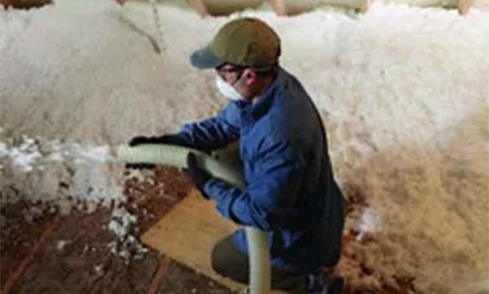 Person in protective gear installing blown insulation in attic.