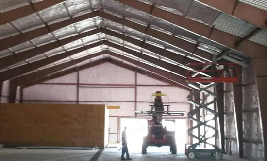 Construction equipment inside a large barn interior with worker nearby