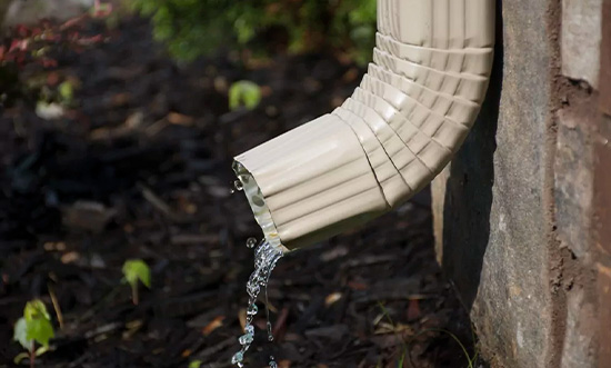 Water flowing from a beige gutter spout attached to a brick wall.