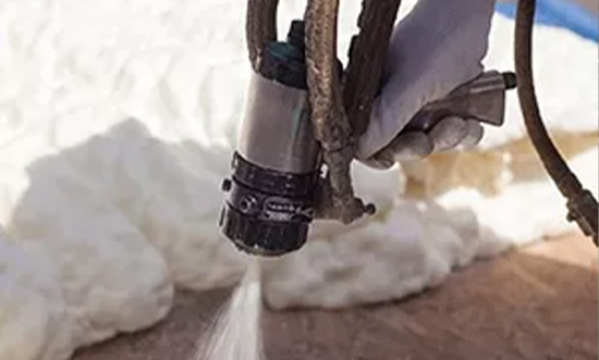 Hand spraying foam insulation onto a surface in a construction setting