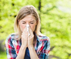 woman sneezing into tissue; Improve Indoor Air Quality with Air Sealing from Delmarva Spray Foam in Georgetown, Delaware