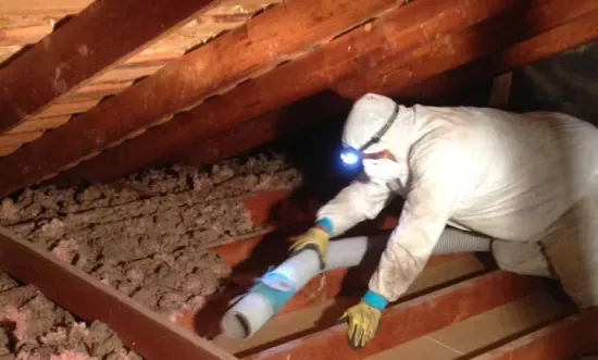 Worker in protective gear removing attic insulation