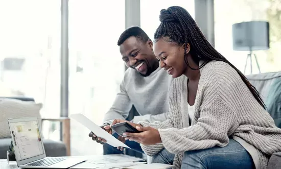 Couple reviewing documents and using tablet, smiling in a bright living room.