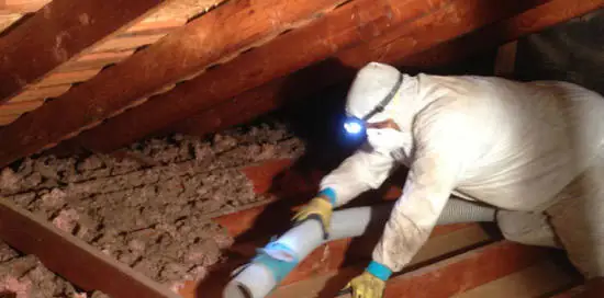 Worker removing insulation in an attic.