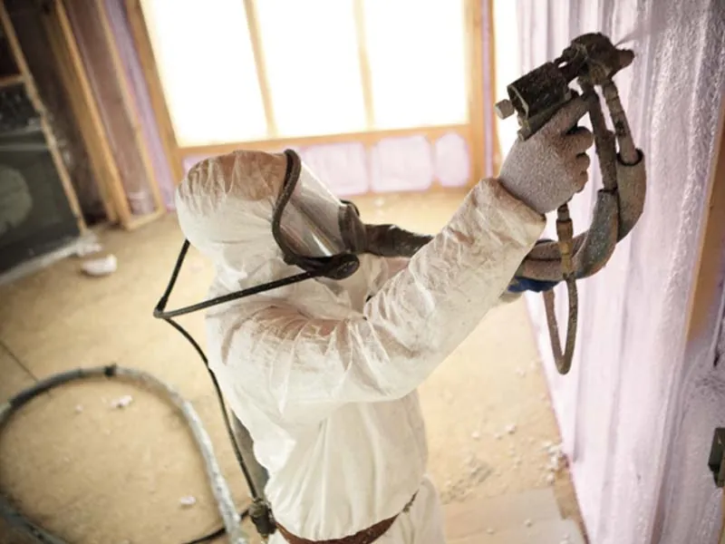 Installer applying spray foam insulation to wall for improved air seal and efficiency.