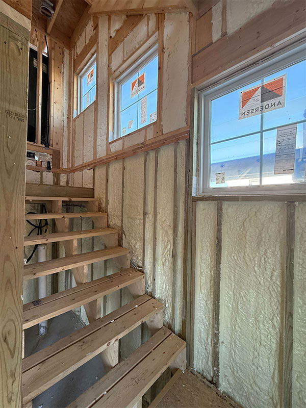 Places-we-install-spray-foam Wooden stairs in a construction area with spray foam insulation on walls and three Andersen windows