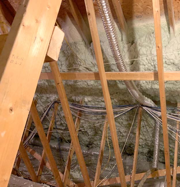 Open-cell spray foam insulation applied to attic roof with exposed rafters and ductwork.