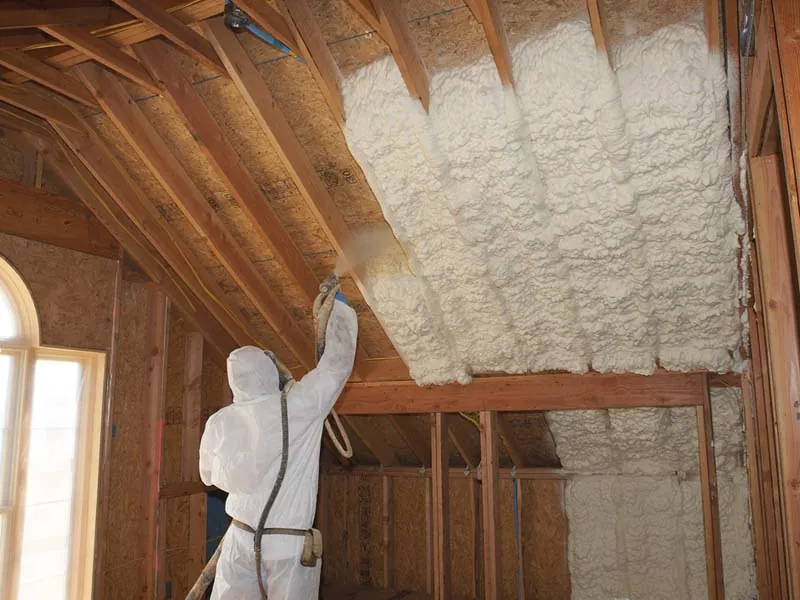 Installer applying spray foam insulation to attic roofline for improved efficiency and air sealing.