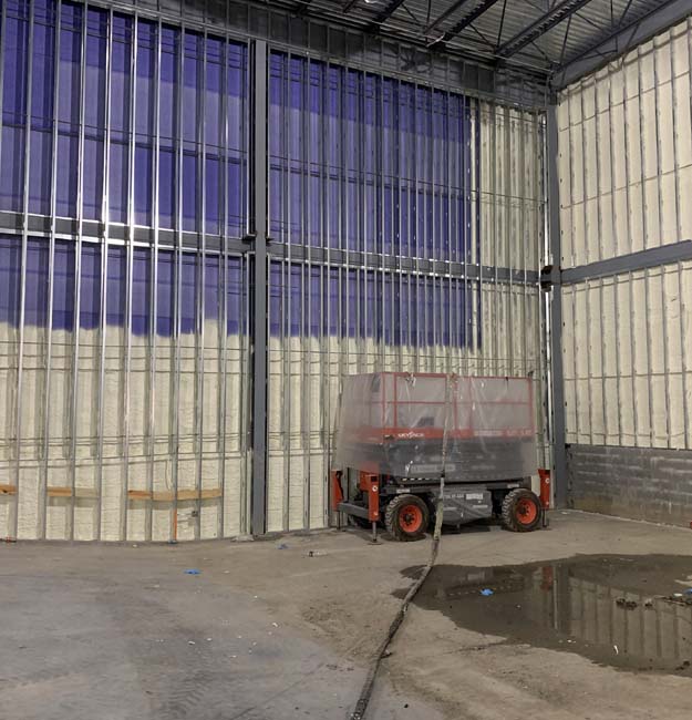 Closed-cell spray foam insulation applied to large commercial metal-framed walls.