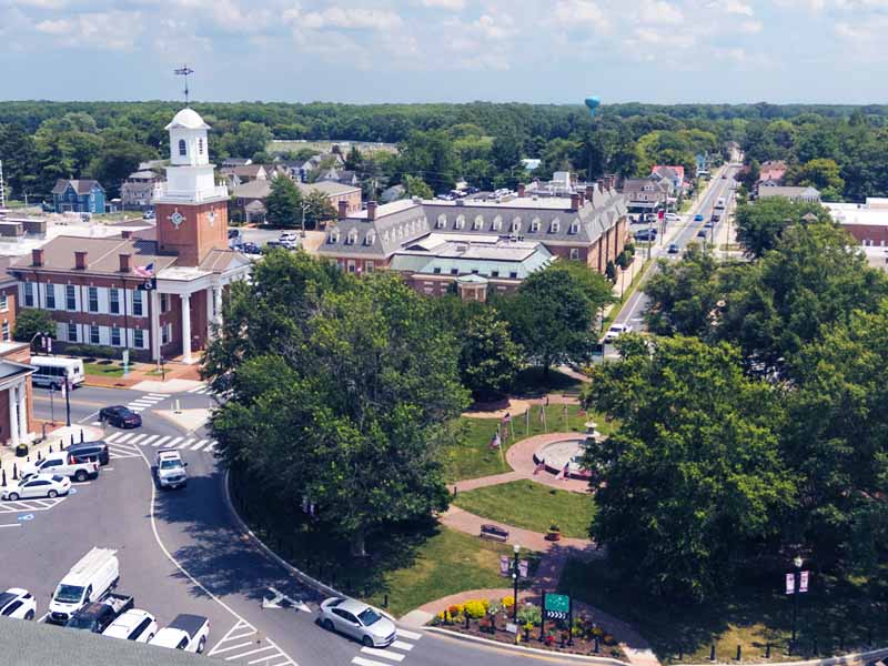 Elevated view of The Circle in Georgetown, Delaware, featuring the Sussex County Courthouse with its white cupola, adjacent government buildings, tree-lined streets, and the roundabout below.