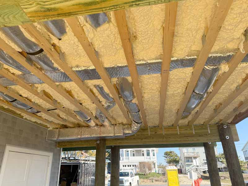Spray foam insulation applied around HVAC ductwork under new home construction.