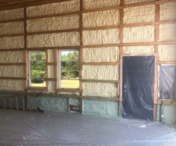 Interior view of a wood-framed wall with spray foam insulation and two windows, during residential construction.