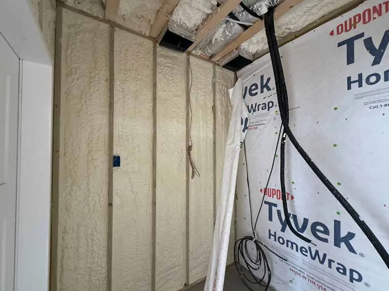 Closed cell spray foam insulation applied to wall studs next to Tyvek HomeWrap in residential construction.