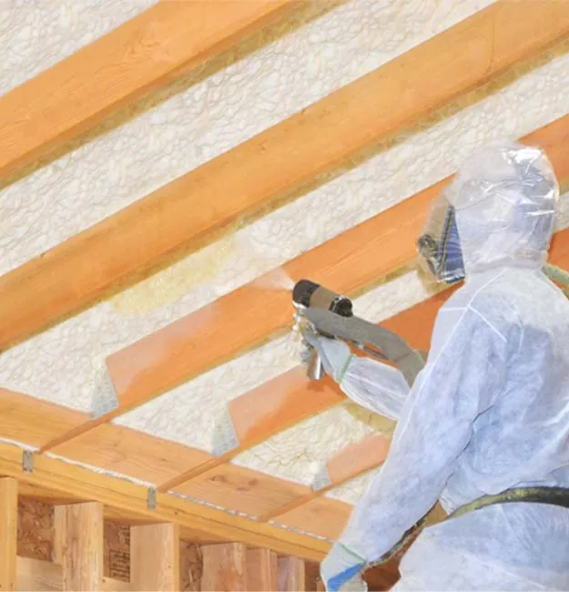 Worker spraying foam insulation between ceiling joists for thermal and air sealing benefits.