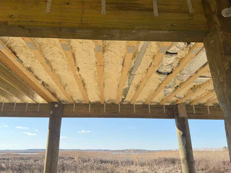 Spray foam insulation applied under subfloor beams during new home construction.