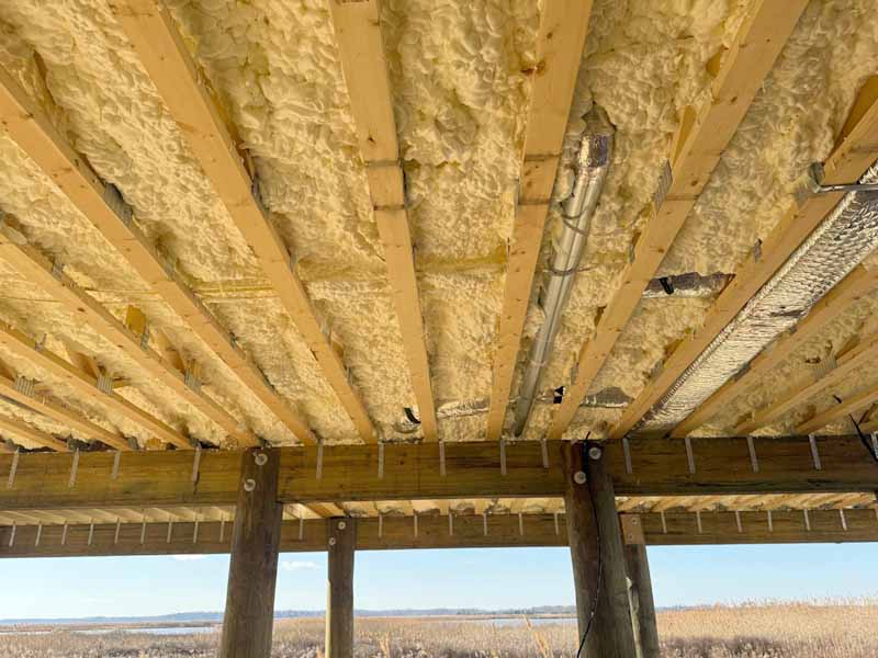 Spray foam insulation applied between wooden floor joists in new home construction.